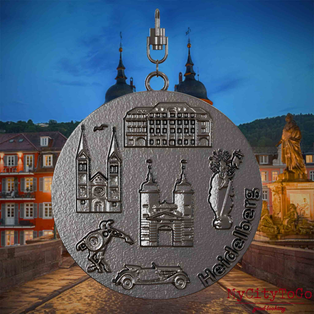 Halskette mit Drehwirbel und Rückseite eines Schmuckanhängers aus Titan, auf dem Reliefs bekannter Sehenswürdigkeiten der Stadt Heidelberg abgebildet sind. Den Hintergrund bildet eine Ansicht der Stadt Heidelberg .
