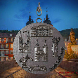 Halskette mit Drehwirbel und Rückseite eines Schmuckanhängers aus Titan, auf dem Reliefs bekannter Sehenswürdigkeiten der Stadt Heidelberg abgebildet sind. Den Hintergrund bildet eine Ansicht der Stadt Heidelberg .
