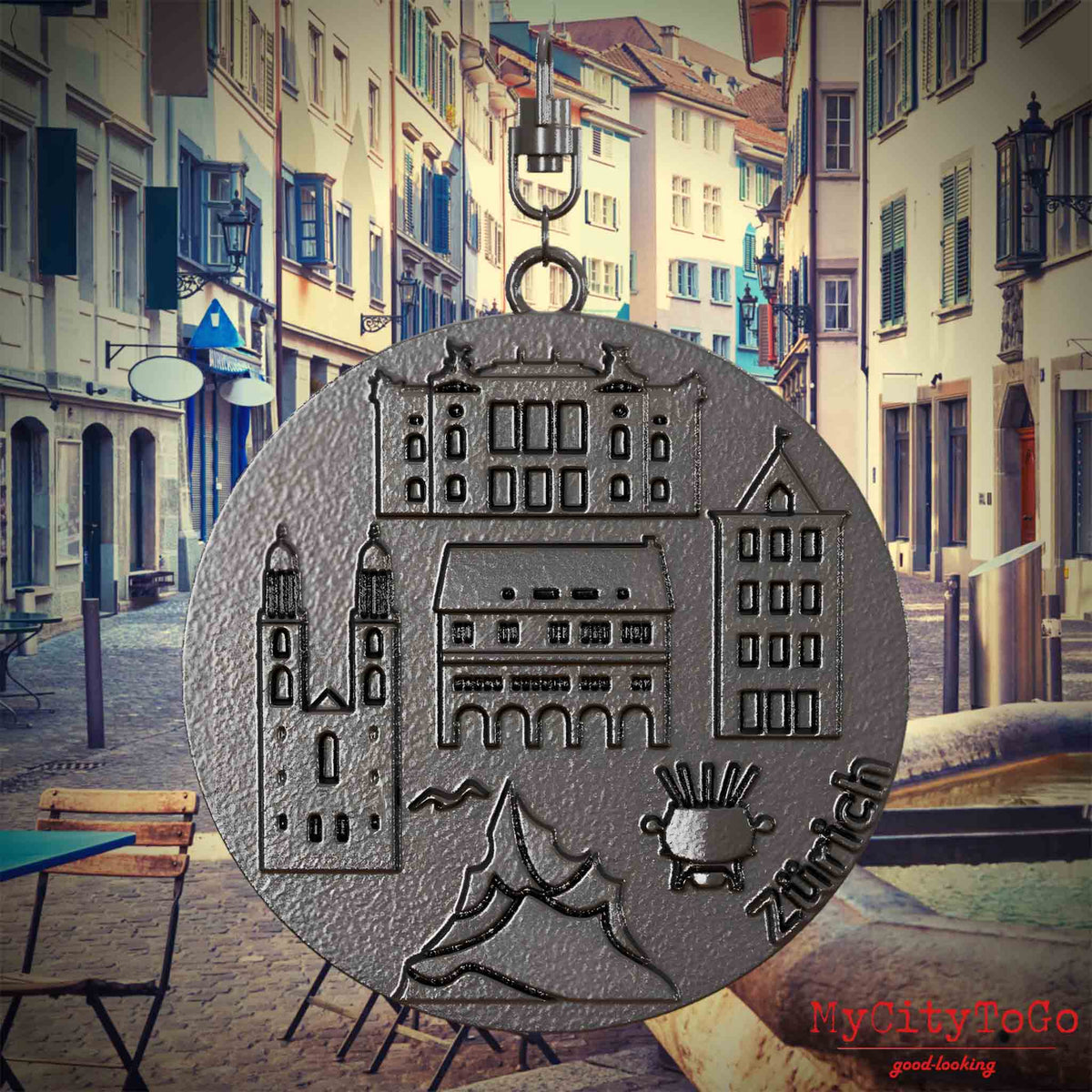 Halskette mit Drehwirbel und Vorderseite eines Schmuckanhängers aus Titan, auf dem Reliefs bekannter Sehenswürdigkeiten der Stadt Zuerich abgebildet sind. Den Hintergrund bildet eine Ansicht der Stadt Zuerich.



