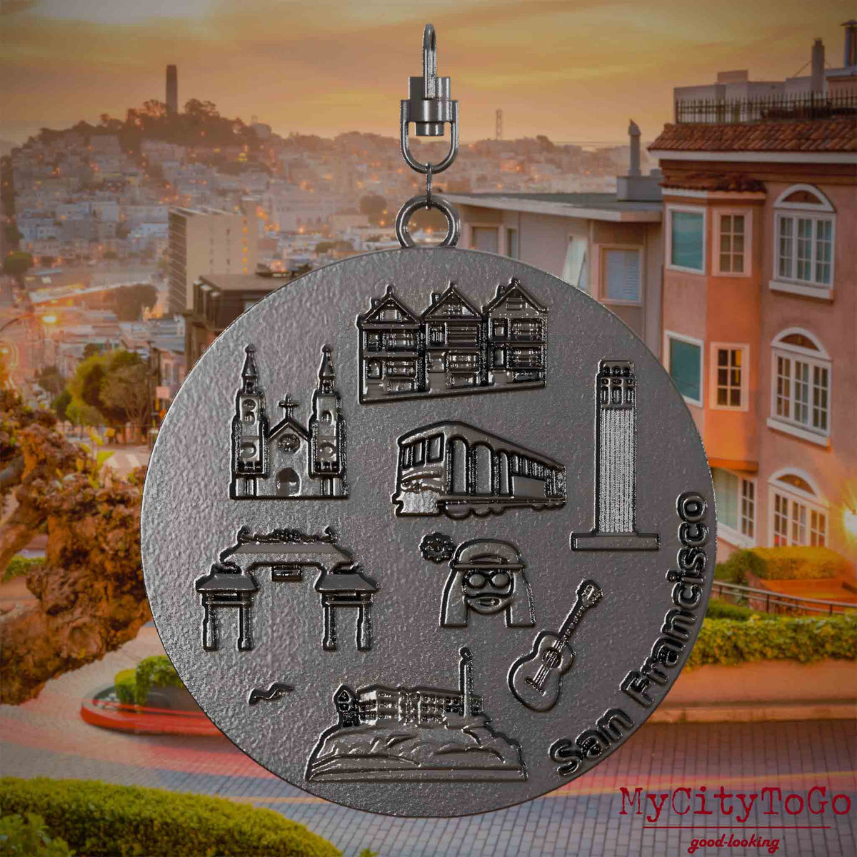 Halskette mit Drehwirbel und Rückseite eines Schmuckanhängers aus Titan, auf dem Reliefs bekannter Sehenswürdigkeiten der Stadt San Francisco abgebildet sind. Den Hintergrund bildet eine Ansicht der Stadt San Francisco.
