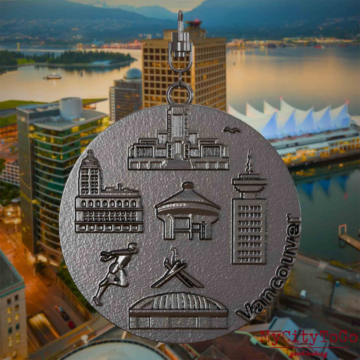 Halskette mit Drehwirbel und Rückseite eines Schmuckanhängers aus Titan, auf dem Reliefs bekannter Sehenswürdigkeiten der Stadt Vancouver abgebildet sind. Den Hintergrund bildet eine Ansicht der Stadt Vancouver.
