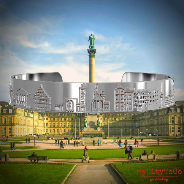 Versilberter Armreif mit Reliefs bekannter Sehenswürdigkeiten der Stadt Stuttgart. Den Hintergrund bildet eine Ansicht der Stadt Stuttgart.