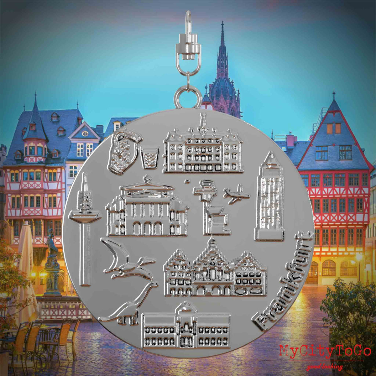 Halskette mit Drehwirbel und Rückseite eines silbernen Schmuckanhängers, auf dem Reliefs bekannter Sehenswürdigkeiten der Stadt Frankfurt abgebildet sind. Den Hintergrund bildet eine Ansicht der Stadt Frankfurt.