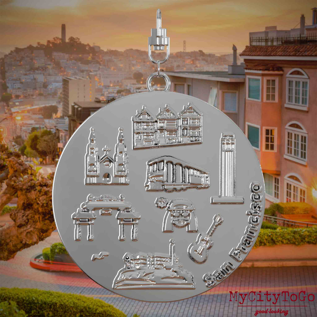 Halskette mit Drehwirbel und Rückseite eines silbernen Schmuckanhängers, auf dem Reliefs bekannter Sehenswürdigkeiten der Stadt San Francisco abgebildet sind. Den Hintergrund bildet eine Ansicht der Stadt San Francisco.
