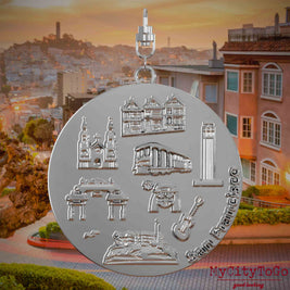 Halskette mit Drehwirbel und Rückseite eines silbernen Schmuckanhängers, auf dem Reliefs bekannter Sehenswürdigkeiten der Stadt San Francisco abgebildet sind. Den Hintergrund bildet eine Ansicht der Stadt San Francisco.
