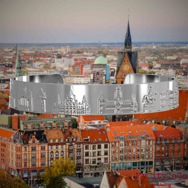Versilberter Armreif mit Reliefs bekannter Sehenswürdigkeiten der Stadt Hannover. Den Hintergrund bildet eine Ansicht der Stadt Hannover.