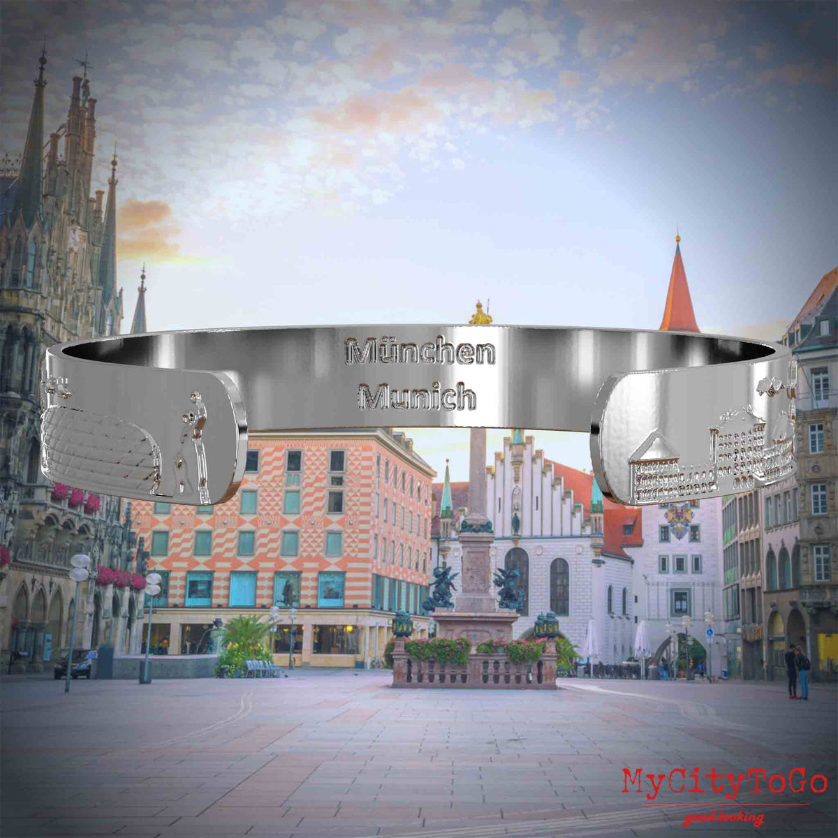 Innenseite eines versilberten Armreifs mit Reliefs beliebter Sehenswürdigkeiten der Stadt Müchen und einer Gravur des Stadtnamens in deutsch und englisch. Den Hintergrund bildet eine Ansicht der Stadt Muenchen.