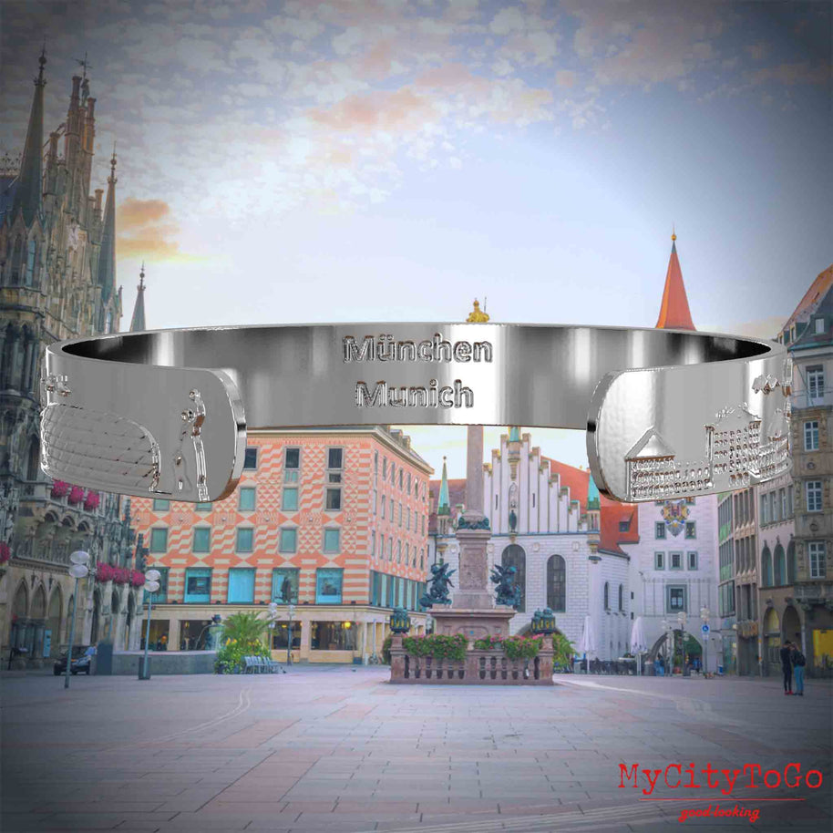 Innenseite eines versilberten Armreifs mit Reliefs beliebter Sehenswürdigkeiten der Stadt Müchen und einer Gravur des Stadtnamens in deutsch und englisch. Den Hintergrund bildet eine Ansicht der Stadt Muenchen.