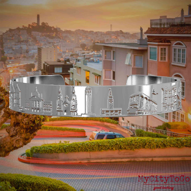 Versilberter Armreif mit Reliefs bekannter Sehenswürdigkeiten der Stadt San Francisco. Den Hintergrund bildet eine Ansicht der Stadt San Francisco.