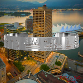 Versilberter Armreif mit Reliefs bekannter Sehenswürdigkeiten der Stadt Vancouver. Den Hintergrund bildet eine Ansicht der Stadt Vancouver.