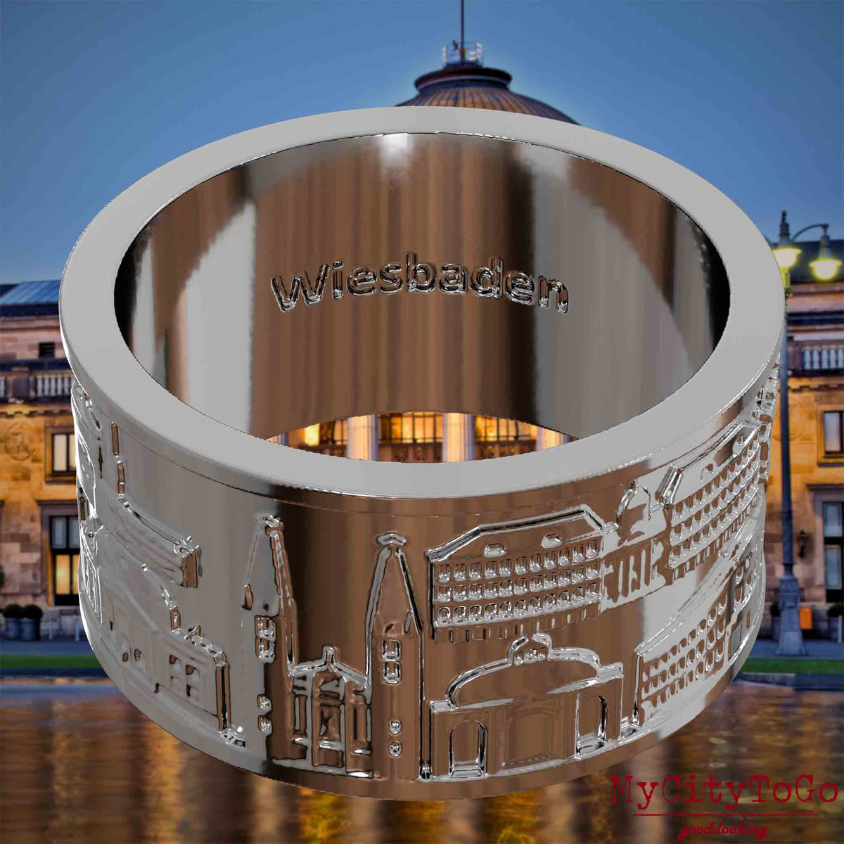 Versilberter Ring mit Reliefs bekannter Sehenswürdigkeiten der Stadt Wiesbaden und einer Gravur des Stadtnamens auf der Innenseite. Den Hintergrund bildet eine Ansicht der Stadt Wiesbaden.