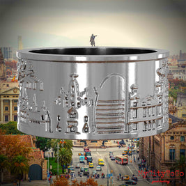 Silberner Ring mit Reliefs bekannter Sehenswürdigkeiten der Stadt Barcelona. Den Hintergrund bildet eine Ansicht der Stadt Barcelona.