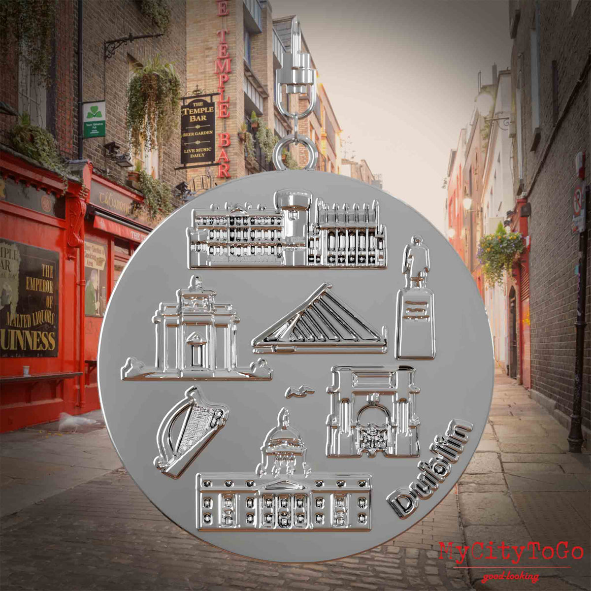Halskette mit Drehwirbel und Rückseite eines silbernen Schmuckanhängers, auf dem Reliefs bekannter Sehenswürdigkeiten der Stadt Dublin abgebildet sind. Den Hintergrund bildet eine Ansicht der Stadt Dublin.

