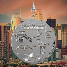 Halskette mit Drehwirbel und Rückseite eines silbernen Schmuckanhängers, auf dem Reliefs bekannter Sehenswürdigkeiten der Stadt Los Angeles abgebildet sind. Den Hintergrund bildet eine Ansicht der Stadt Los Angeles.

