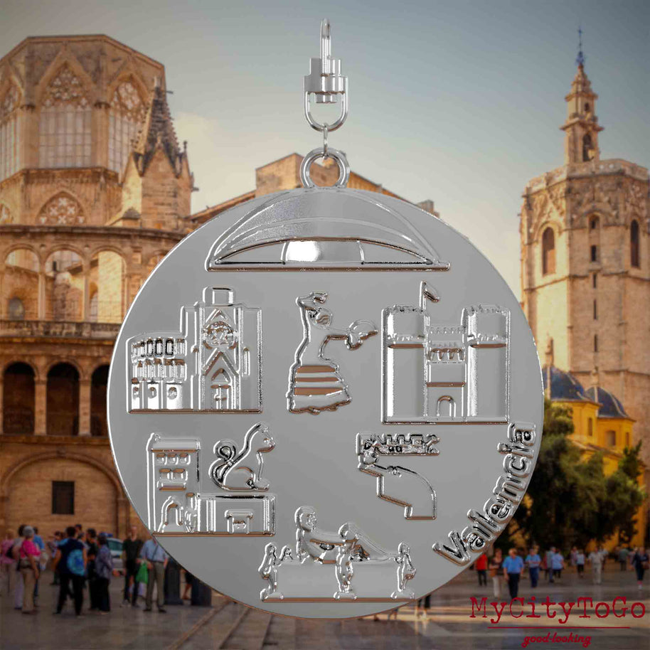 Halskette mit Drehwirbel und Rückseite eines vergoldeten Schmuckanhängers, auf dem Reliefs bekannter Sehenswürdigkeiten der Stadt Valencia abgebildet sind. Den Hintergrund bildet eine Ansicht der Stadt Valencia.

