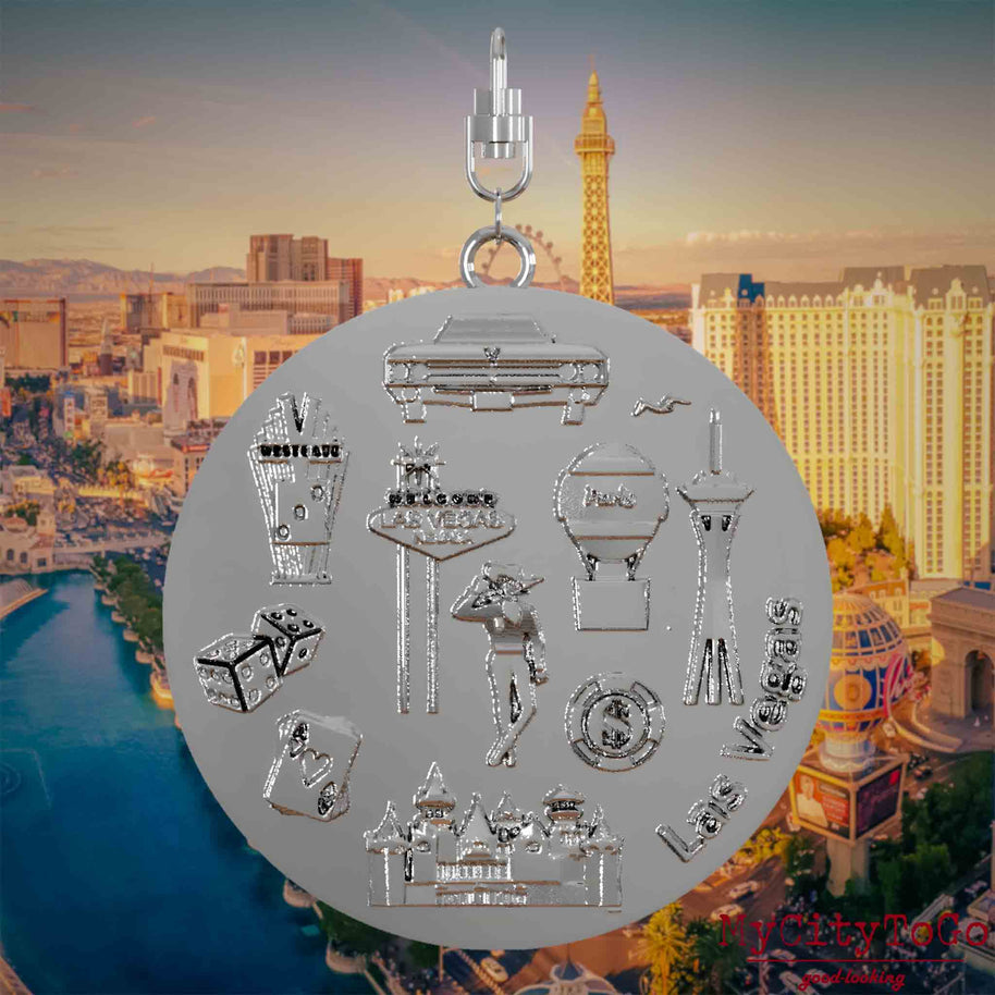 Halskette mit Drehwirbel und Rückseite eines silbernen Schmuckanhängers, auf dem Reliefs bekannter Sehenswürdigkeiten der Stadt Las Vegas abgebildet sind. Den Hintergrund bildet eine Ansicht der Stadt Las Vegas.
