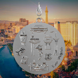 Halskette mit Drehwirbel und Rückseite eines silbernen Schmuckanhängers, auf dem Reliefs bekannter Sehenswürdigkeiten der Stadt Las Vegas abgebildet sind. Den Hintergrund bildet eine Ansicht der Stadt Las Vegas.
