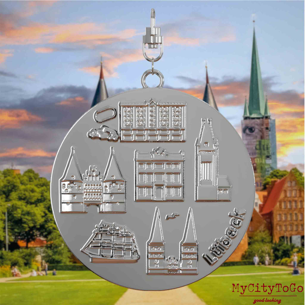 Halskette mit Drehwirbel und Rückseite eines silbernen Schmuckanhängers, auf dem Reliefs bekannter Sehenswürdigkeiten der Stadt Luebeck abgebildet sind. Den Hintergrund bildet eine Ansicht der Stadt Luebeck.
