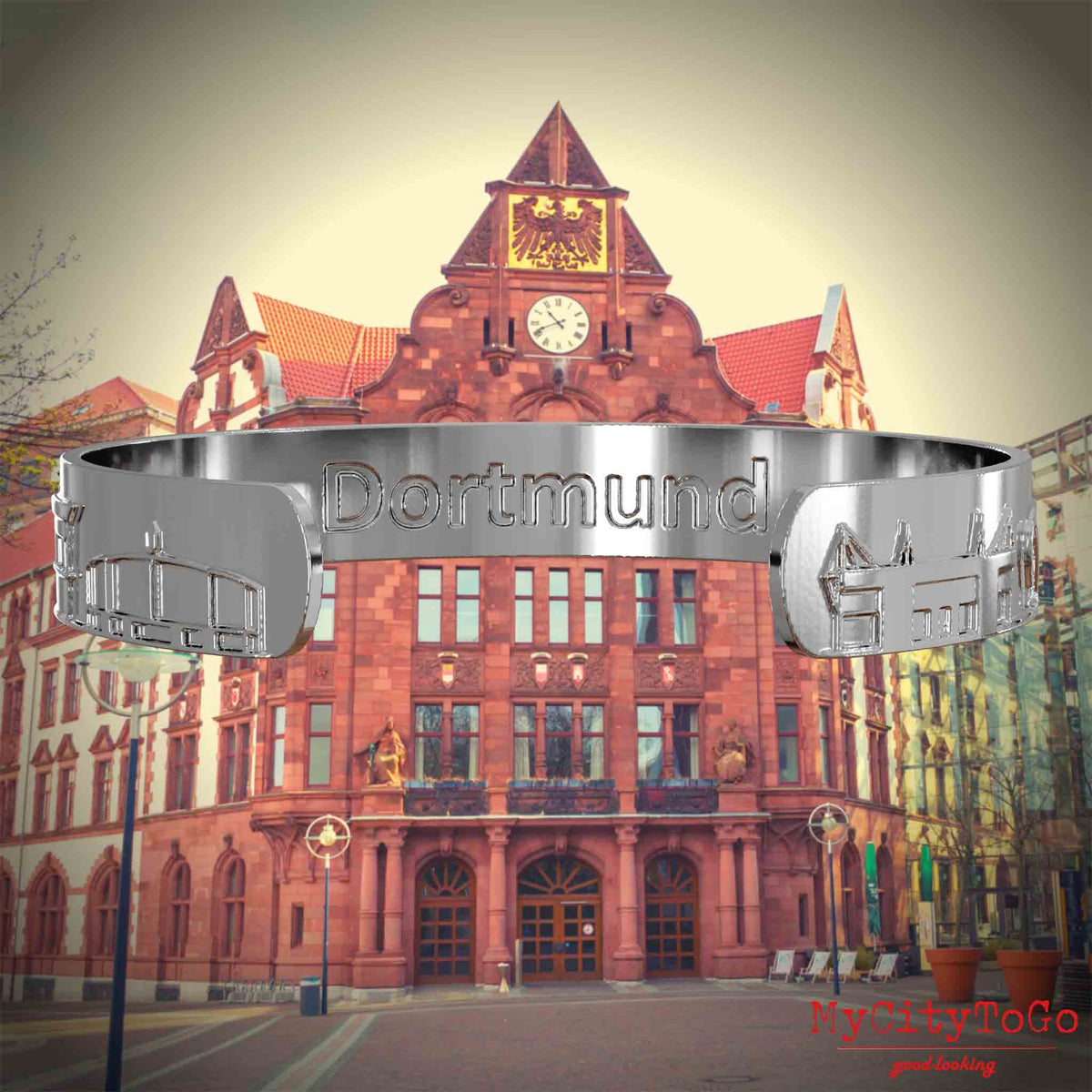 Innenseite eines silbernen Armreifs mit Reliefs bekannter Sehenswürdigkeiten der Stadt Dortmund und einer Gravur des Stadtnamens. Den Hintergrund bildet eine Ansicht der Stadt Dortmund.