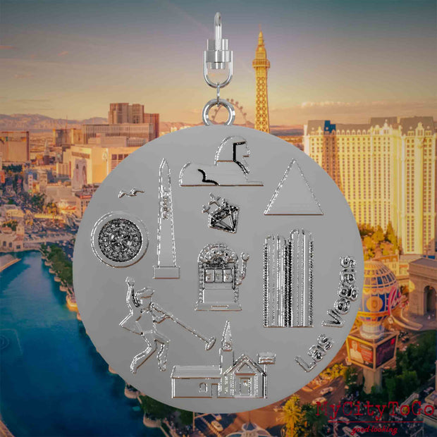 Halskette mit Drehwirbel und Vorderseite eines silbernen Schmuckanhängers, auf dem Reliefs bekannter Sehenswürdigkeiten der Stadt Las Vegas abgebildet sind. Den Hintergrund bildet eine Ansicht der Stadt Las Vegas.
