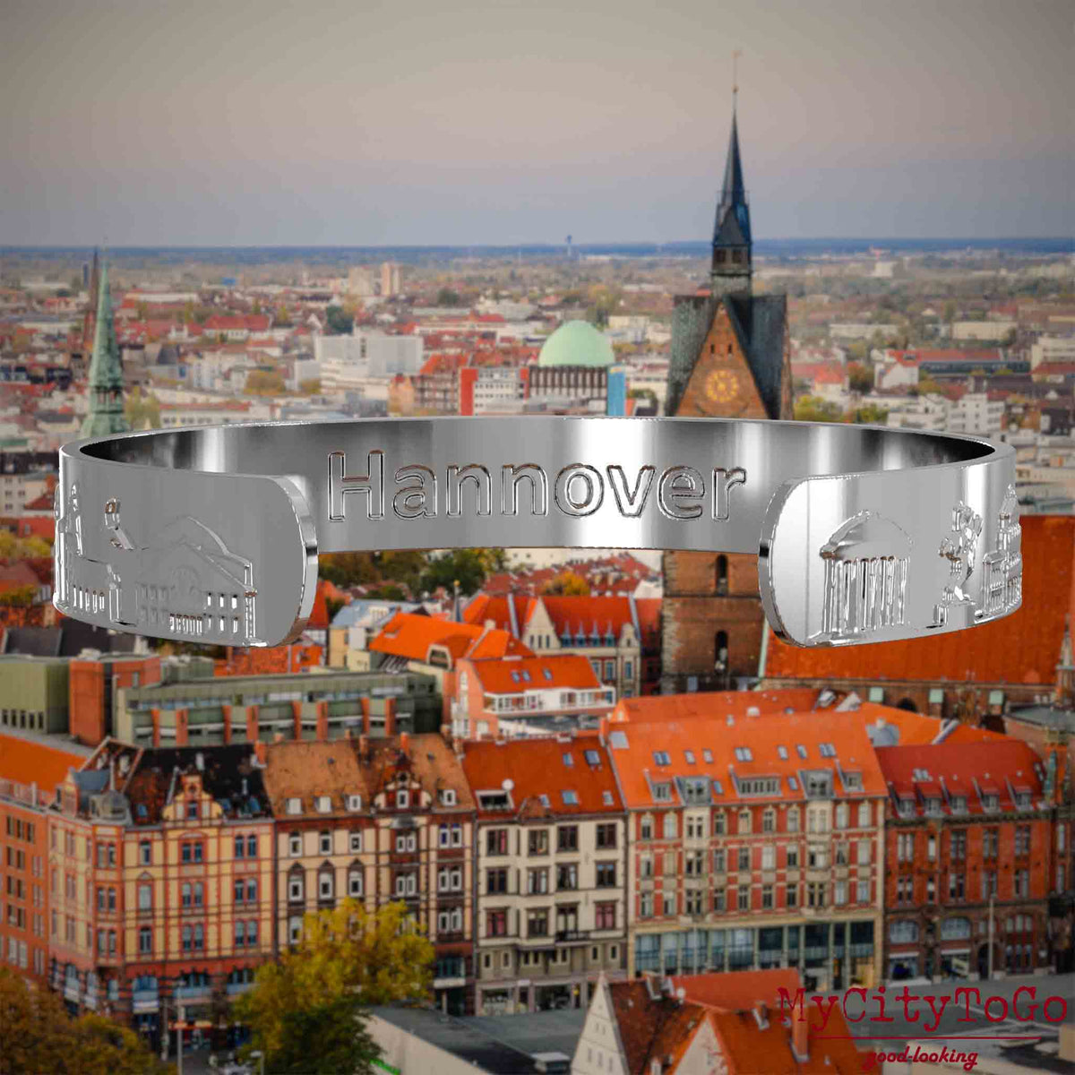Innenseite eines silbernen Armreifs mit Reliefs bekannter Sehenswürdigkeiten der Stadt Hannover und einer Gravur des Stadtnamens. Den Hintergrund bildet eine Ansicht der Stadt Hannover.