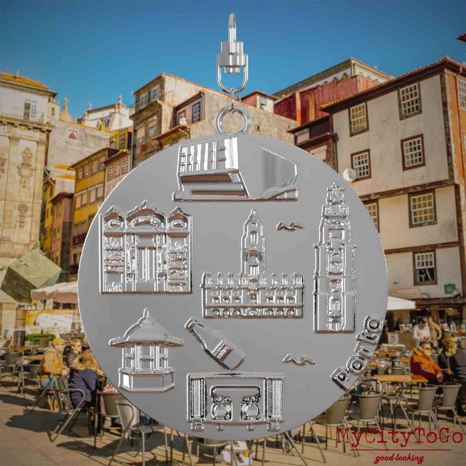 Halskette mit Drehwirbel und Vorderseite eines silbernen Schmuckanhängers, auf dem Reliefs bekannter Sehenswürdigkeiten der Stadt Porto abgebildet sind. Den Hintergrund bildet eine Ansicht der Stadt Porto.
