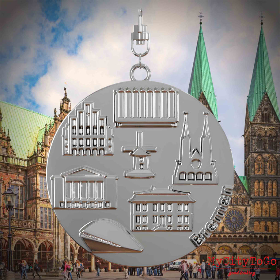 Halskette mit Drehwirbel und Rückseite eines silbernen Schmuckanhängers, auf dem Reliefs bekannter Sehenswürdigkeiten der Stadt Bremen abgebildet sind. Den Hintergrund bildet eine Ansicht der Stadt Bremen.