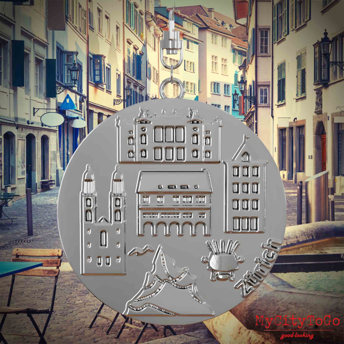 Halskette mit Drehwirbel und Vorderseite eines silbernen Schmuckanhängers, auf dem Reliefs bekannter Sehenswürdigkeiten der Stadt Zuerich abgebildet sind. Den Hintergrund bildet eine Ansicht der Stadt Zuerich.

