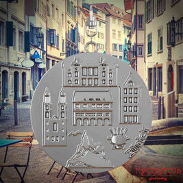 Halskette mit Drehwirbel und Vorderseite eines silbernen Schmuckanhängers, auf dem Reliefs bekannter Sehenswürdigkeiten der Stadt Zuerich abgebildet sind. Den Hintergrund bildet eine Ansicht der Stadt Zuerich.
