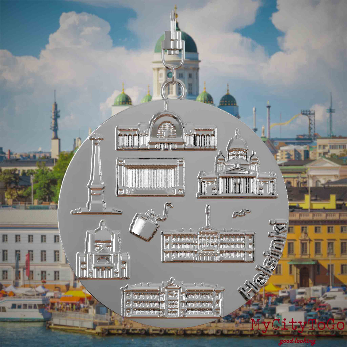 Halskette mit Drehwirbel und Vorderseite eines silbernen Schmuckanhängers, auf dem Reliefs bekannter Sehenswürdigkeiten der Stadt Helsinki abgebildet sind. Den Hintergrund bildet eine Ansicht der Stadt Helsinki .
