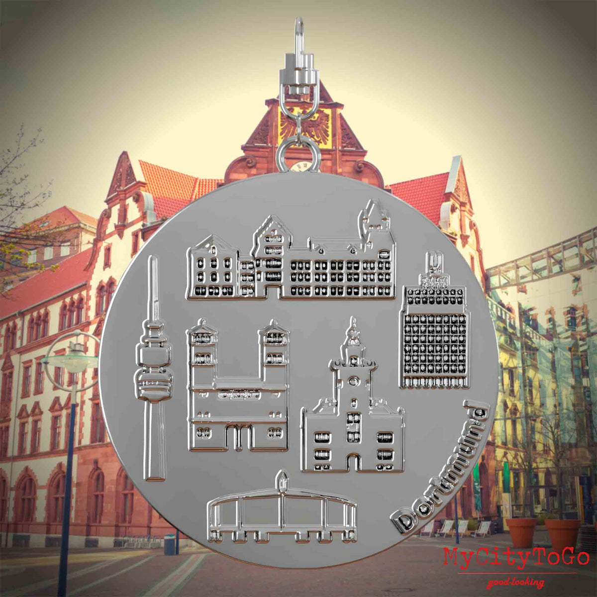 Halskette mit Drehwirbel und Vorderseite eines silbernen Schmuckanhängers, auf dem Reliefs bekannter Sehenswürdigkeiten der Stadt Dortmund abgebildet sind. Den Hintergrund bildet eine Ansicht der Stadt Dortmund.