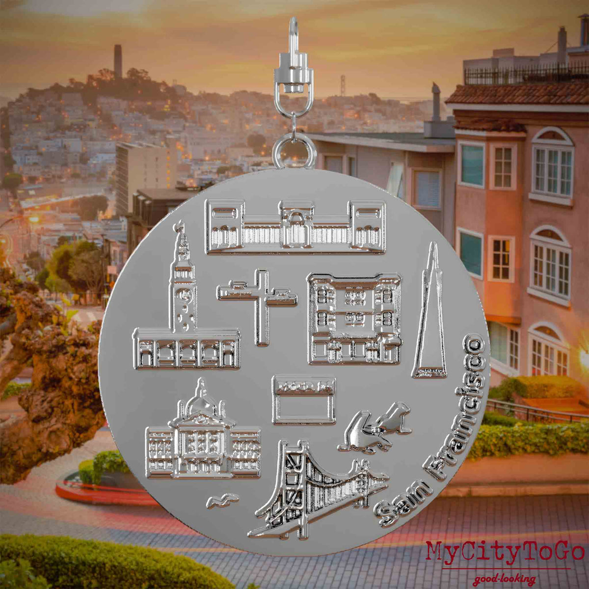 Halskette mit Drehwirbel und Vorderseite eines silbernen Schmuckanhängers, auf dem Reliefs bekannter Sehenswürdigkeiten der Stadt San Francisco abgebildet sind. Den Hintergrund bildet eine Ansicht der Stadt San Francisco.
