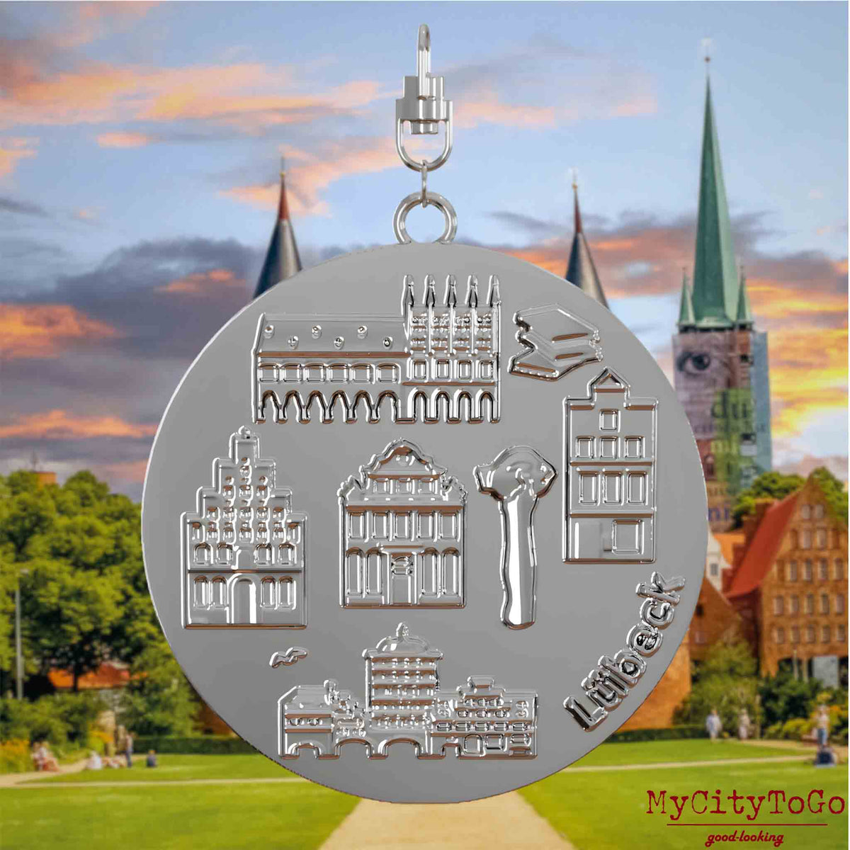 Halskette mit Drehwirbel und Vorderseite eines silbernen Schmuckanhängers, auf dem Reliefs bekannter Sehenswürdigkeiten der Stadt Luebeck abgebildet sind. Den Hintergrund bildet eine Ansicht der Stadt Luebeck.
