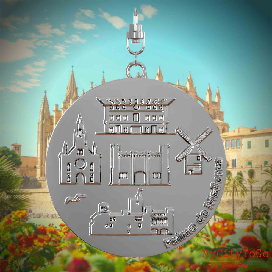 Halskette mit Drehwirbel und Vorderseite eines silbernen Schmuckanhängers, auf dem Reliefs bekannter Sehenswürdigkeiten der Stadt Palma de Mallorca abgebildet sind. Den Hintergrund bildet eine Ansicht der Stadt Palma de Mallorca.
