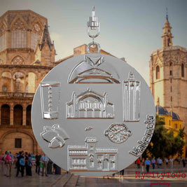 Halskette mit Drehwirbel und Vorderseite eines silbernen Schmuckanhängers, auf dem Reliefs bekannter Sehenswürdigkeiten der Stadt Valencia abgebildet sind. Den Hintergrund bildet eine Ansicht der Stadt Valencia.
