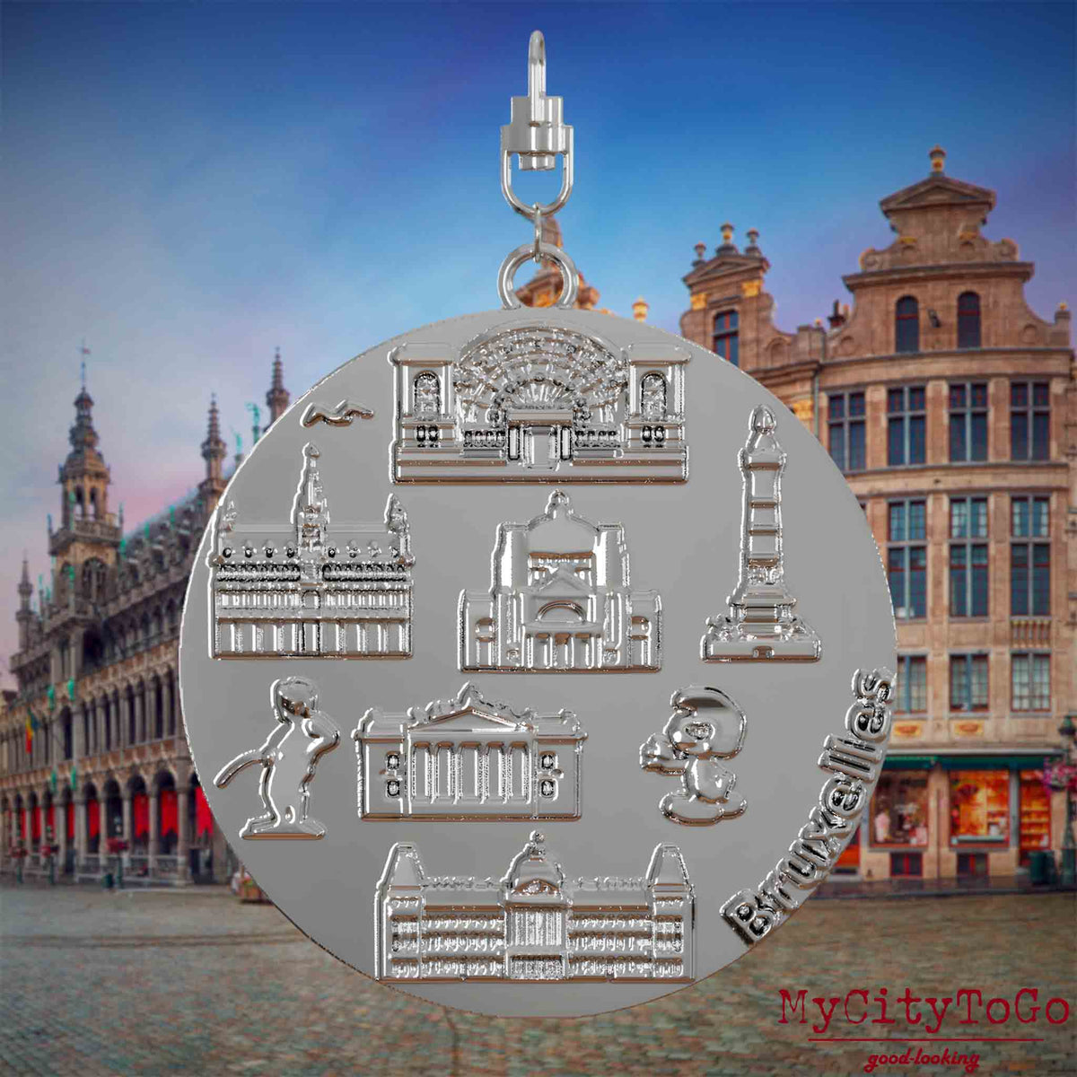 Halskette mit Drehwirbel und Vorderseite eines silbernen Schmuckanhängers, auf dem Reliefs bekannter Sehenswürdigkeiten der Stadt Bruessel abgebildet sind. Den Hintergrund bildet eine Ansicht der Stadt Bruessel.
