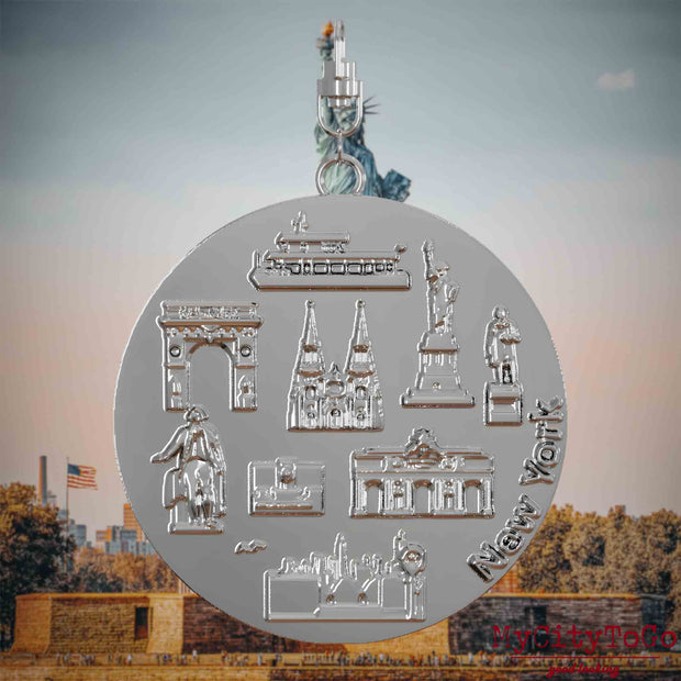 Halskette mit Drehwirbel und Vorderseite eines silbernen Schmuckanhängers, auf dem Reliefs bekannter Sehenswürdigkeiten der Stadt New York abgebildet sind. Den Hintergrund bildet eine Ansicht der Stadt New York.
