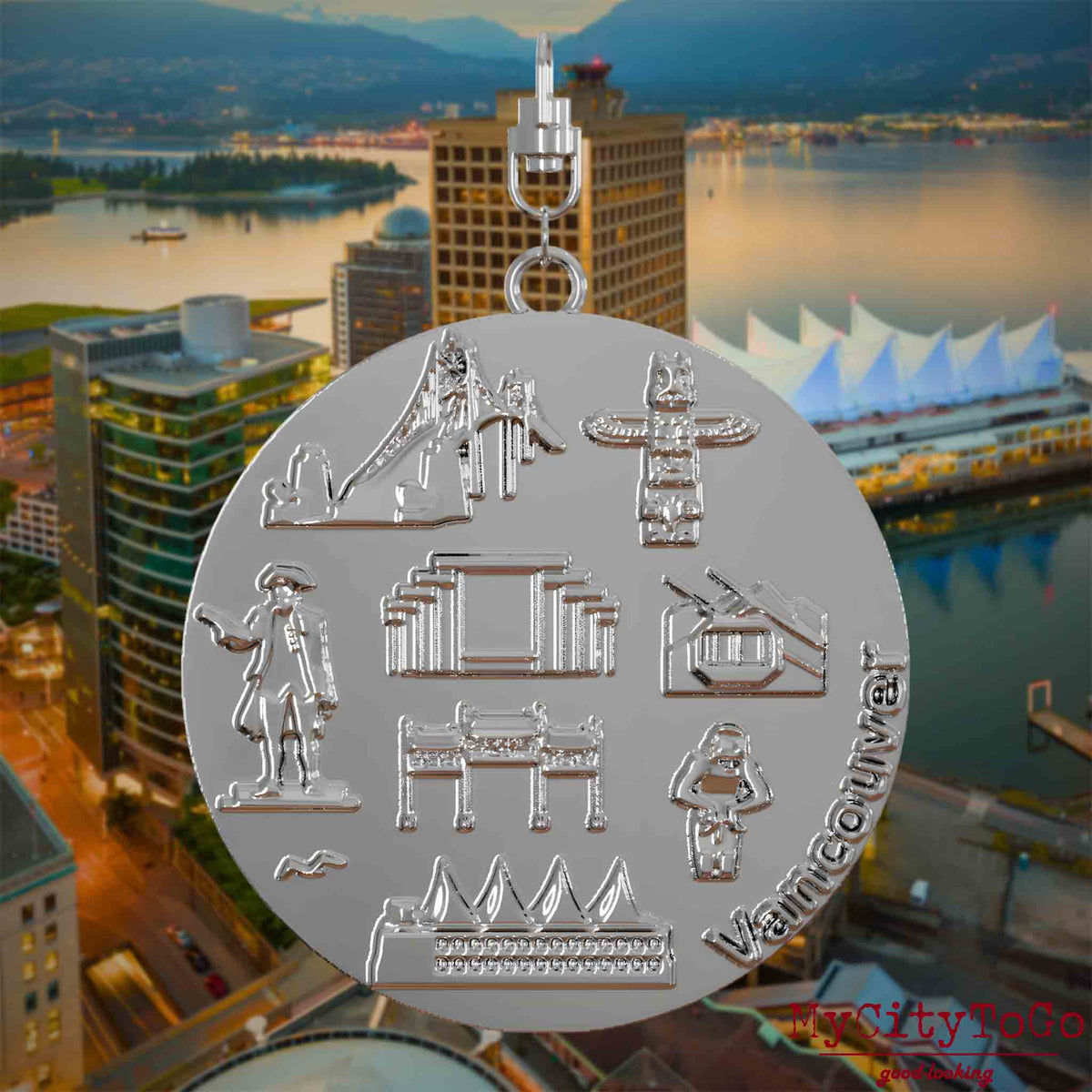 Halskette mit Drehwirbel und Vorderseite eines silbernen Schmuckanhängers, auf dem Reliefs bekannter Sehenswürdigkeiten der Stadt Vancouver abgebildet sind. Den Hintergrund bildet eine Ansicht der Stadt Vancouver.
