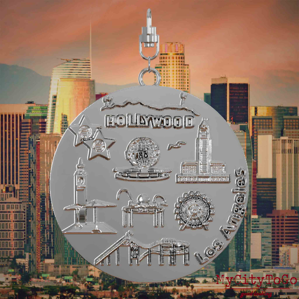 Halskette mit Drehwirbel und Vorderseite eines silbernen Schmuckanhängers, auf dem Reliefs bekannter Sehenswürdigkeiten der Stadt Los Angeles abgebildet sind. Den Hintergrund bildet eine Ansicht der Stadt Los Angeles.
