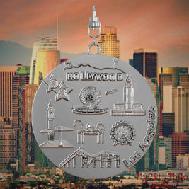 Halskette mit Drehwirbel und Vorderseite eines silbernen Schmuckanhängers, auf dem Reliefs bekannter Sehenswürdigkeiten der Stadt Los Angeles abgebildet sind. Den Hintergrund bildet eine Ansicht der Stadt Los Angeles.
