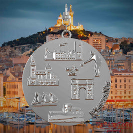 Halskette mit Drehwirbel und Vorderseite eines silbernen Schmuckanhängers, auf dem Reliefs bekannter Sehenswürdigkeiten der Stadt Marseille abgebildet sind. Den Hintergrund bildet eine Ansicht der Stadt Marseille.
