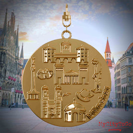 Halskette mit Drehwirbel und Vorderseite eines vergoldeten Schmuckanhängers, auf dem Reliefs bekannter Sehenswürdigkeiten der Stadt Muenchen abgebildet sind. Den Hintergrund bildet eine Ansicht der Stadt Muenchen.
