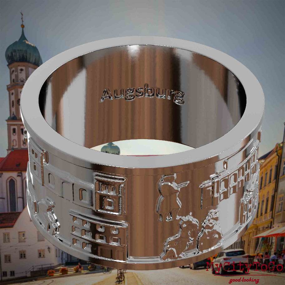 Versilberter Ring mit Reliefs bekannter Sehenswürdigkeiten der Stadt Augsburg und einer Gravur des Stadtnamens auf der Innenseite. Den Hintergrund bildet eine Ansicht der Stadt Augsburg.