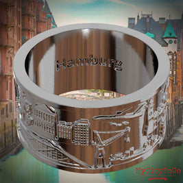 Versilberter Ring mit Reliefs bekannter Sehenswürdigkeiten der Stadt Hamburg und einer Gravur des Stadtnamens auf der Innenseite. Den Hintergrund bildet eine Ansicht der Stadt Hamburg.