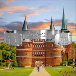 Innenseite eines silbernen Armreifs mit Reliefs bekannter Sehenswürdigkeiten der Stadt Luebeck und einer Gravur des Stadtnamens. Den Hintergrund bildet eine Ansicht der Stadt Luebeck.