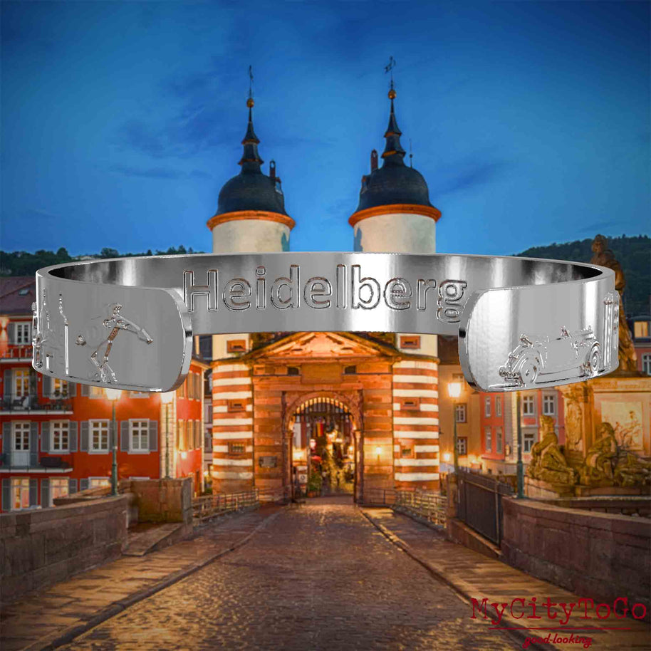 Innenseite eines silbernen Armreifs mit Reliefs bekannter Sehenswürdigkeiten der Stadt Heidelberg und einer Gravur des Stadtnamens. Den Hintergrund bildet eine Ansicht der Stadt Heidelberg.
