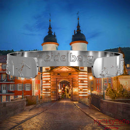 Innenseite eines silbernen Armreifs mit Reliefs bekannter Sehenswürdigkeiten der Stadt Heidelberg und einer Gravur des Stadtnamens. Den Hintergrund bildet eine Ansicht der Stadt Heidelberg.