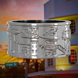 Silberner Ring mit Reliefs bekannter Sehenswürdigkeiten der Stadt Miami. Den Hintergrund bildet eine Ansicht der Stadt Miami.