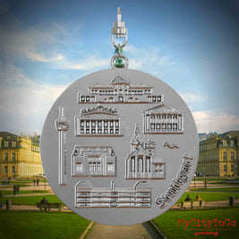 Halskette mit Drehwirbel und Vorderseite eines silbernen Schmuckanhängers, auf dem Reliefs bekannter Sehenswürdigkeiten der Stadt Stuttgart abgebildet sind. Den Hintergrund bildet eine Ansicht der Stadt Stuttgart.

