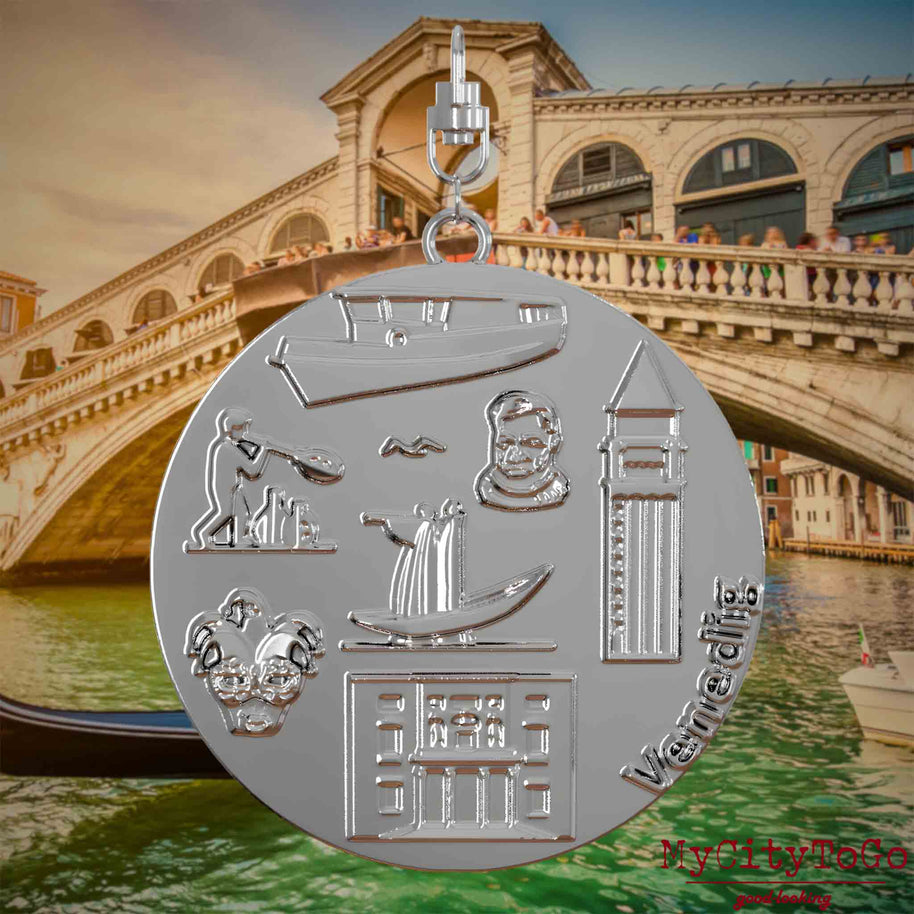 Halskette mit Drehwirbel und Rückseite eines silbernen Schmuckanhängers, auf dem Reliefs bekannter Sehenswürdigkeiten der Stadt Venedig abgebildet sind. Den Hintergrund bildet eine Ansicht der Stadt Venedig.
